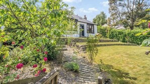 A house with a stone pathway leading to a white door, surrounded by lush greenery and flowering plants. - Garden Cottage Near Edinburgh City Centre NEW (Edinburgh)