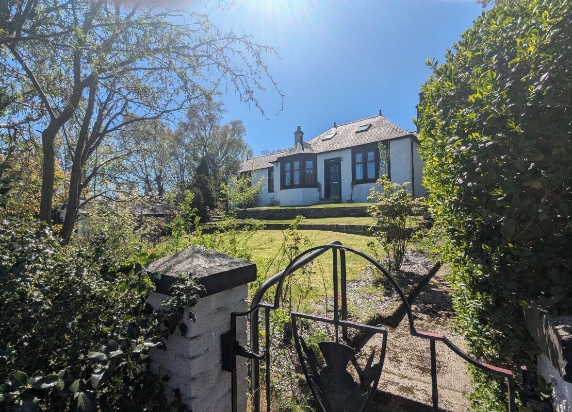 A house with a white exterior, a dark roof, and a front garden with a metal gate.