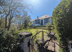 Ein Haus mit weißer Fassade, dunklem Dach und einem Vorgarten mit einem Metallzaun.