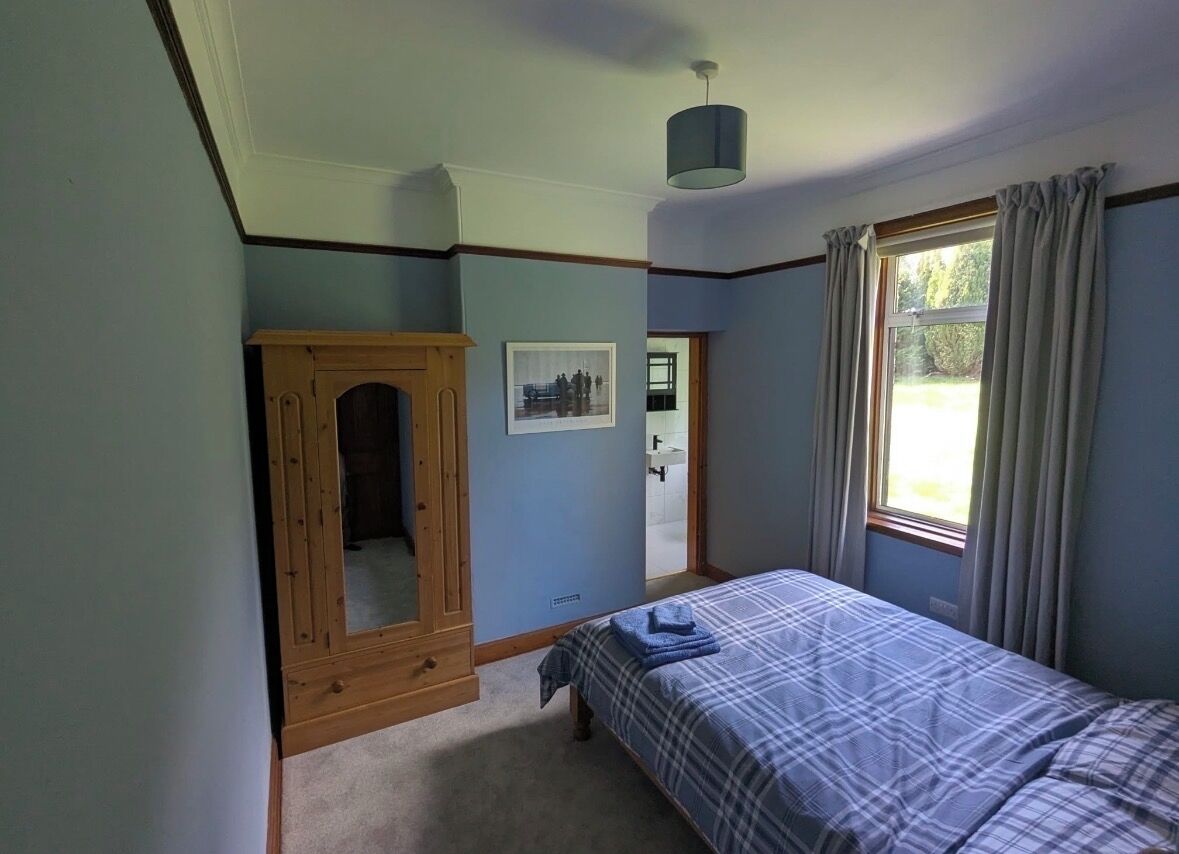Quarto com cama, guarda-roupa de madeira, espelho e janela com cortinas.