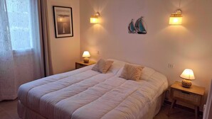 A bedroom with a large bed, two bedside tables with lamps, a framed picture on the wall, and decorative wall art. - Residence close to beaches with terrace and garden (Saint-Coulomb)