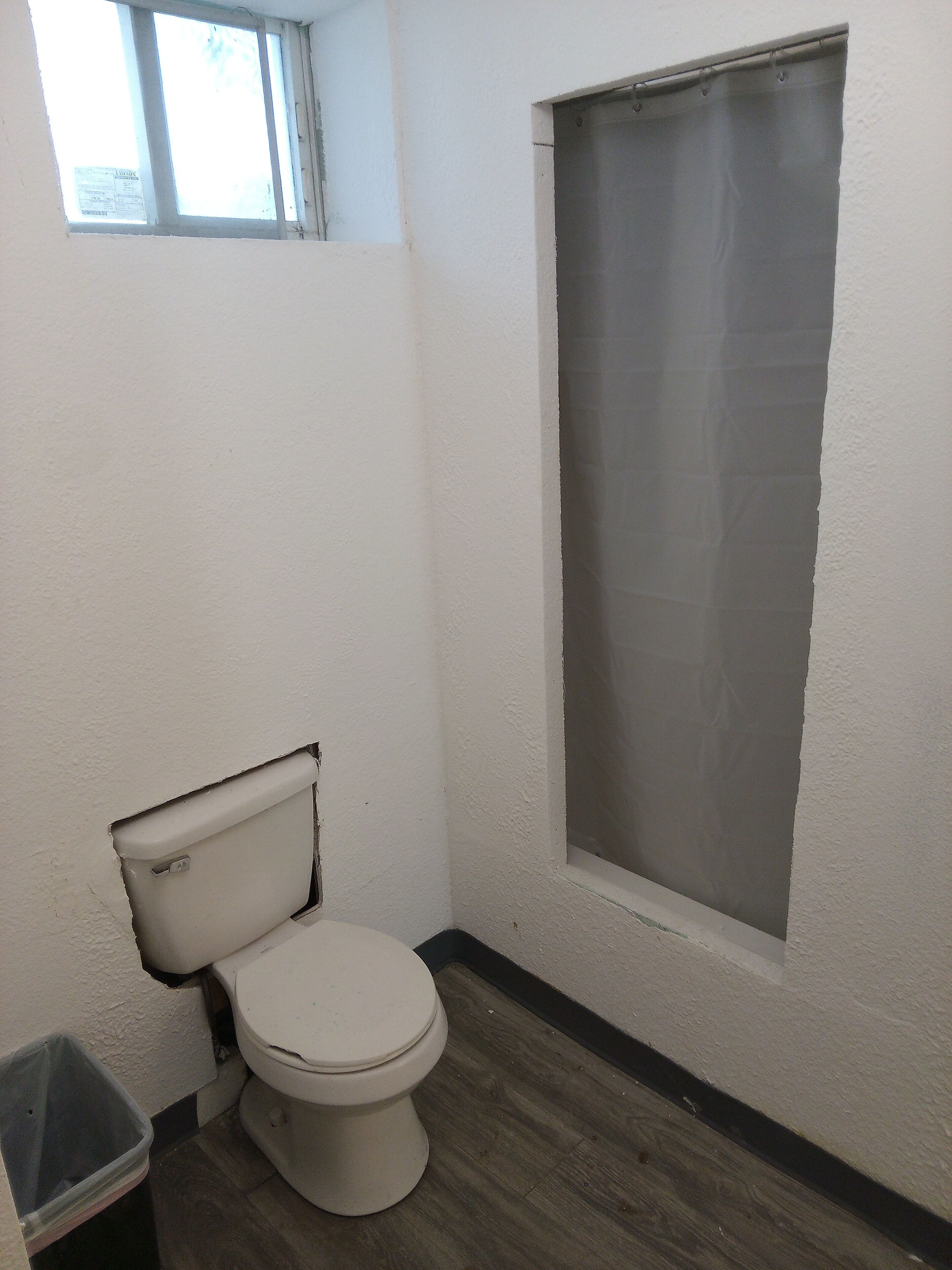 A small bathroom with a toilet, a window, and a shower curtain.