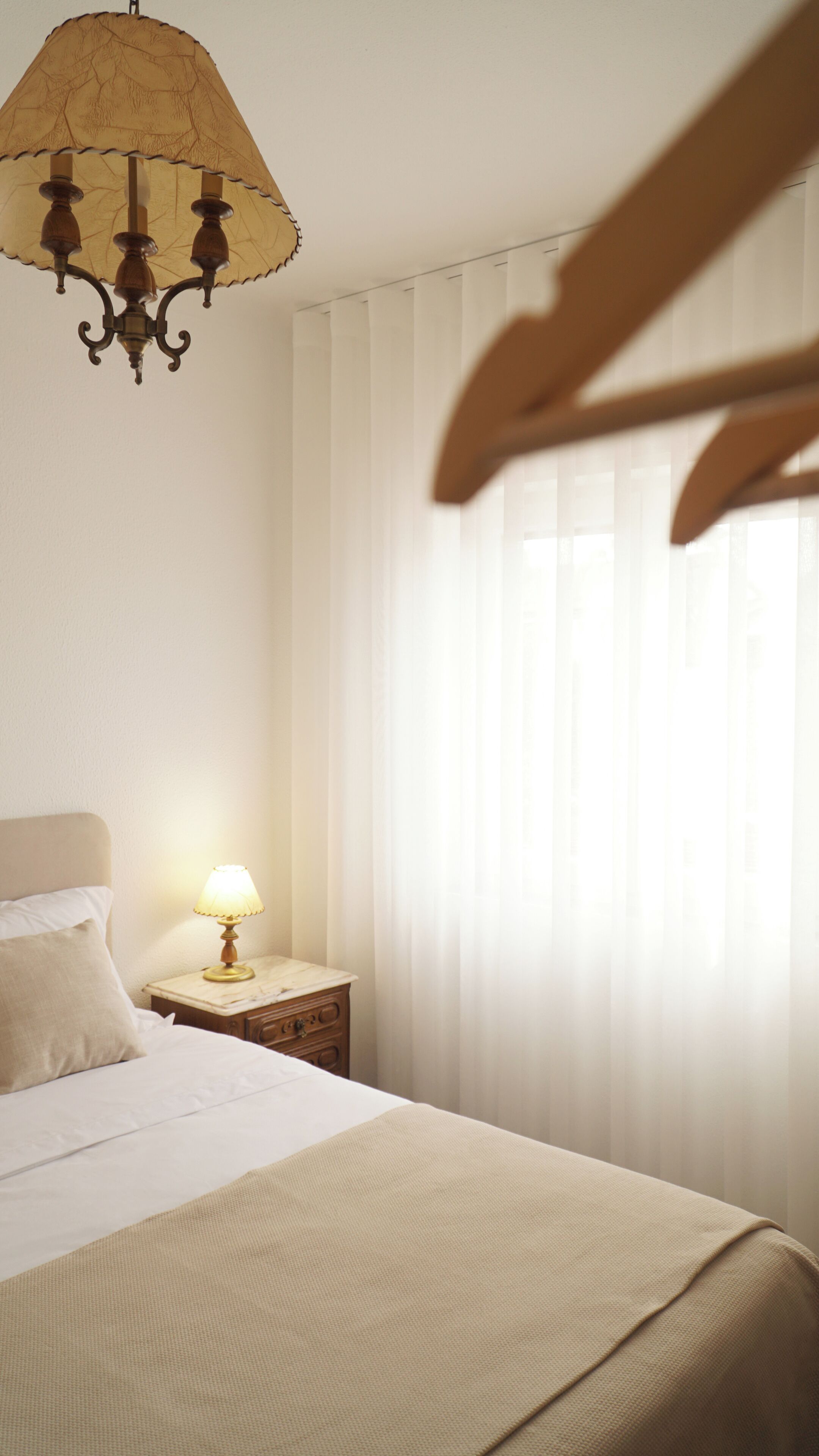 A hotel room with a bed, a nightstand with a lamp, and a chandelier.