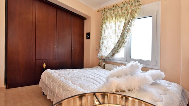 Un dormitori amb un llit, un armari, una finestra amb cortines i una cadira amb una làmpada.