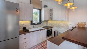 Une cuisine moderne dotée d’un réfrigérateur en acier inoxydable, de meubles en bois, d’une fenêtre, d’un évier, d’un four et de luminaires suspendus.