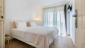 Une chambre à coucher comprenant un lit, une table de chevet, un téléviseur fixé au mur et une fenêtre avec des rideaux.