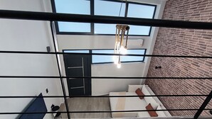A modern interior with a loft-style bed, a brick wall, and large windows. - Zoe Loft ! (Kavala)