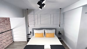 A modern bedroom with a large bed, a brick wall, and a hanging light fixture. - Zoe Loft ! (Kavala)