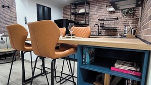 A modern kitchen with a dining area, featuring a brick wall, a blue bookshelf, and a wooden table. - Zoe Loft ! (Kavala)
