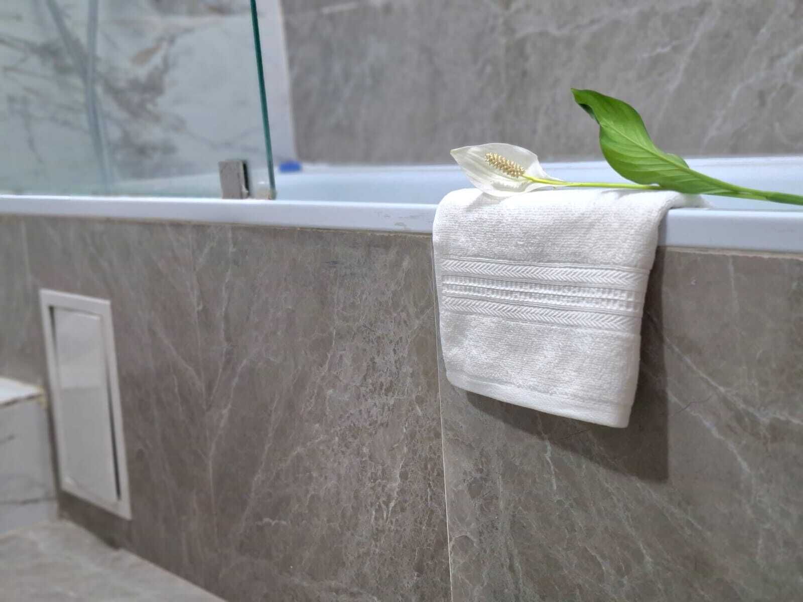A bathroom with a marble wall, a white towel hanging on a towel rack, and a green leaf.