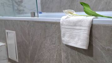 A bathroom with a marble wall, a white towel hanging on a towel rack, and a green leaf.