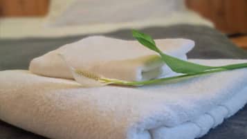 A neatly folded white towel with a green leaf on a bed.