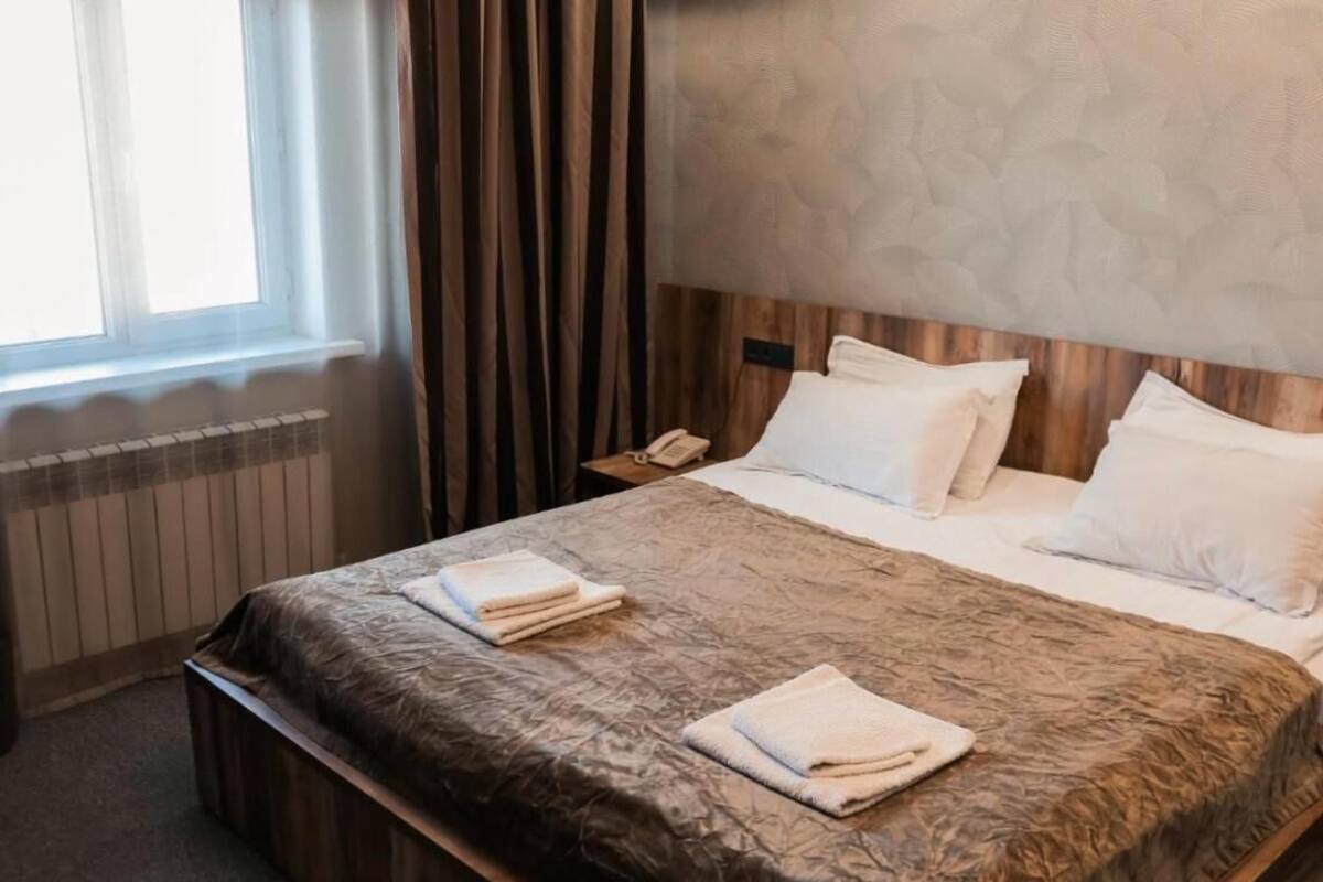 Habitació d'hotel amb un llit, una tauleta de nit, un telèfon i una finestra amb cortines.