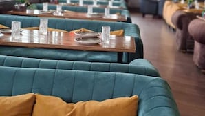 Un ristorante con sedute imbottite color acquamarina, tavoli in legno e decorazioni rosse appese.