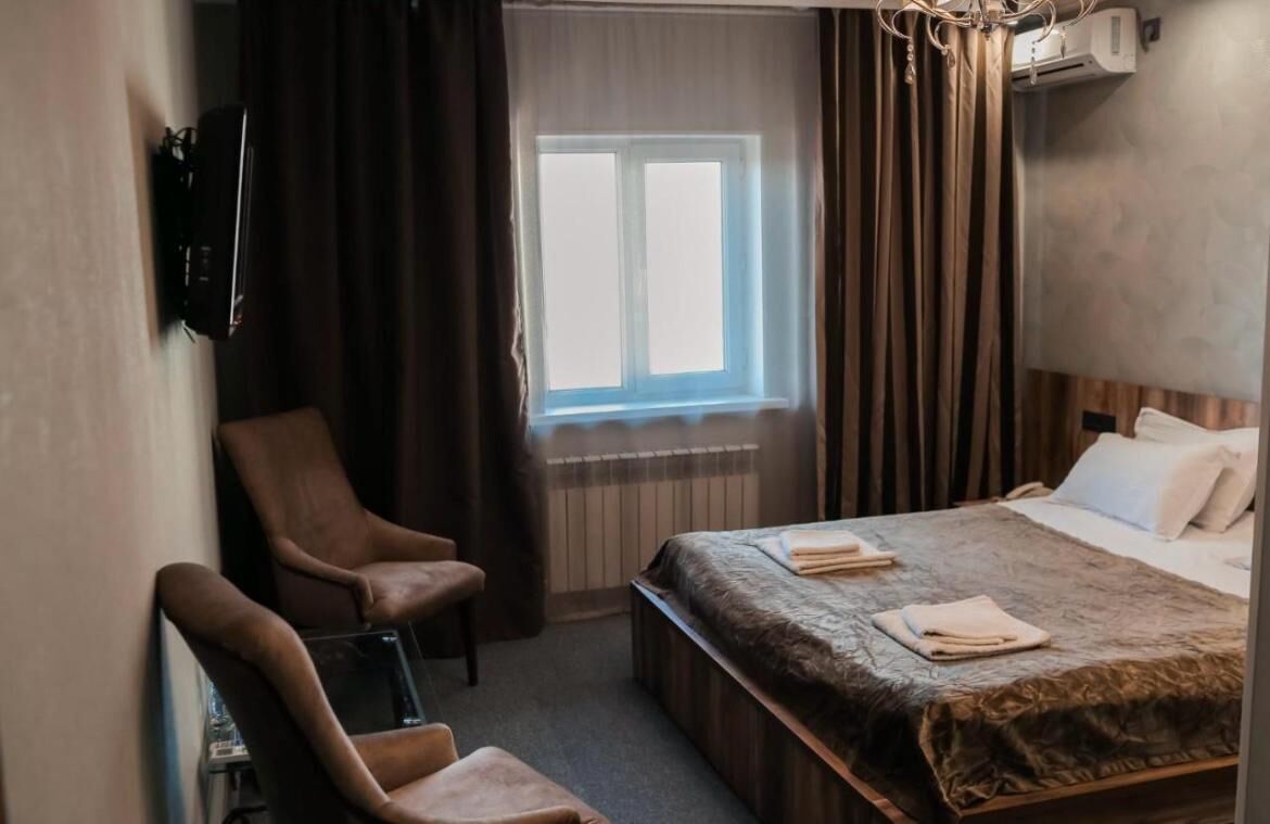 Una habitación de hotel con una cama, una silla, un escritorio, una ventana con cortinas y un equipo de aire acondicionado.