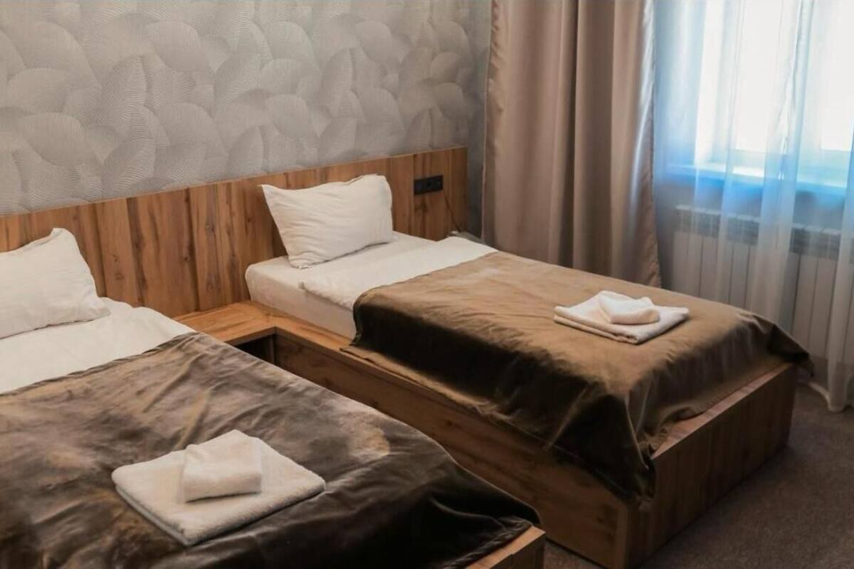 Habitació d'hotel amb dos llits, un panell de fusta al capçal i una finestra amb cortines.