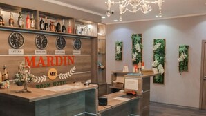 Una reception hotel con orologi che mostrano l'ora in diverse città, un'area accoglienza e un lampadario.