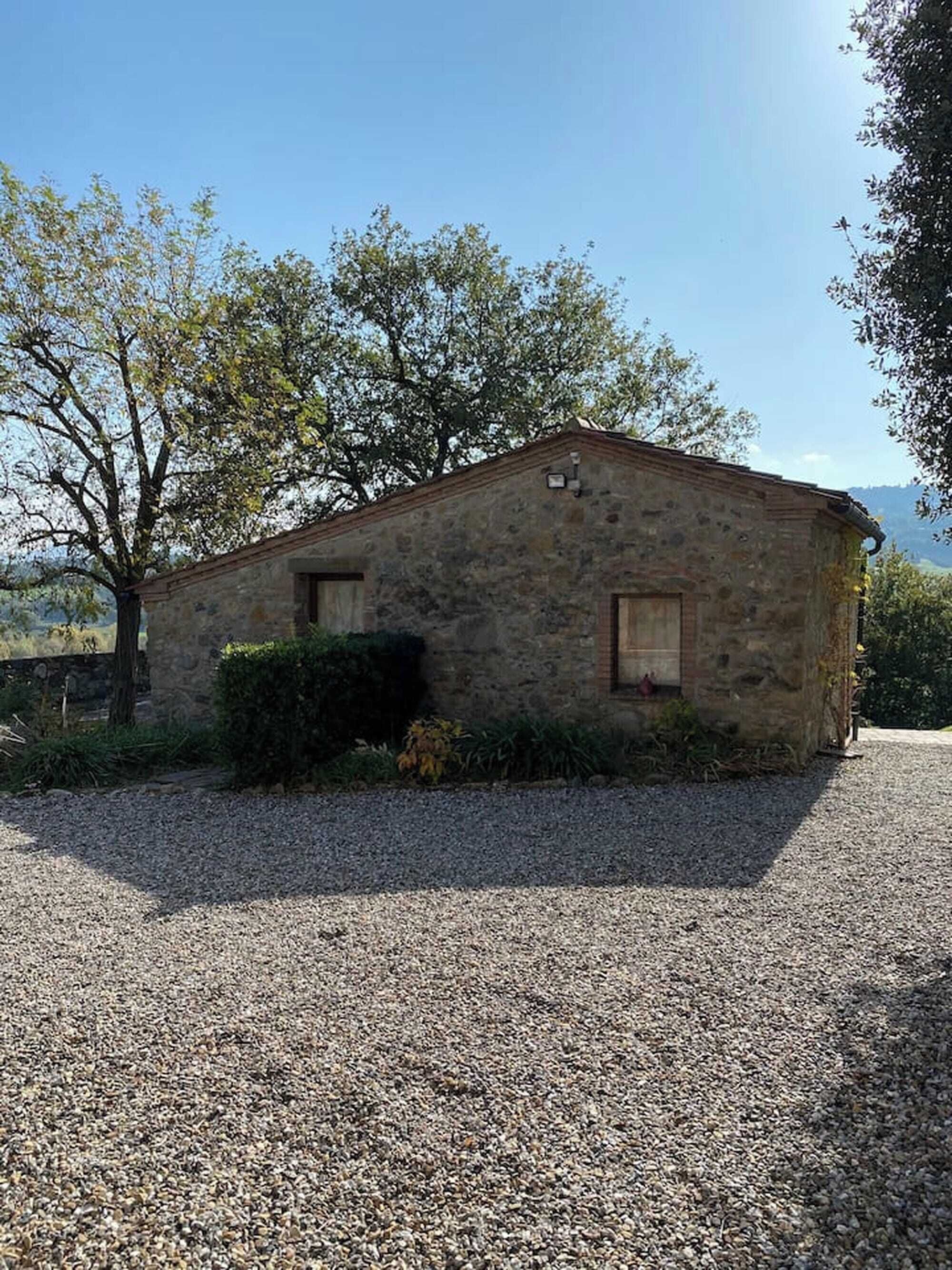 A stone building with a gravel driveway, surrounded by trees and vegetation.