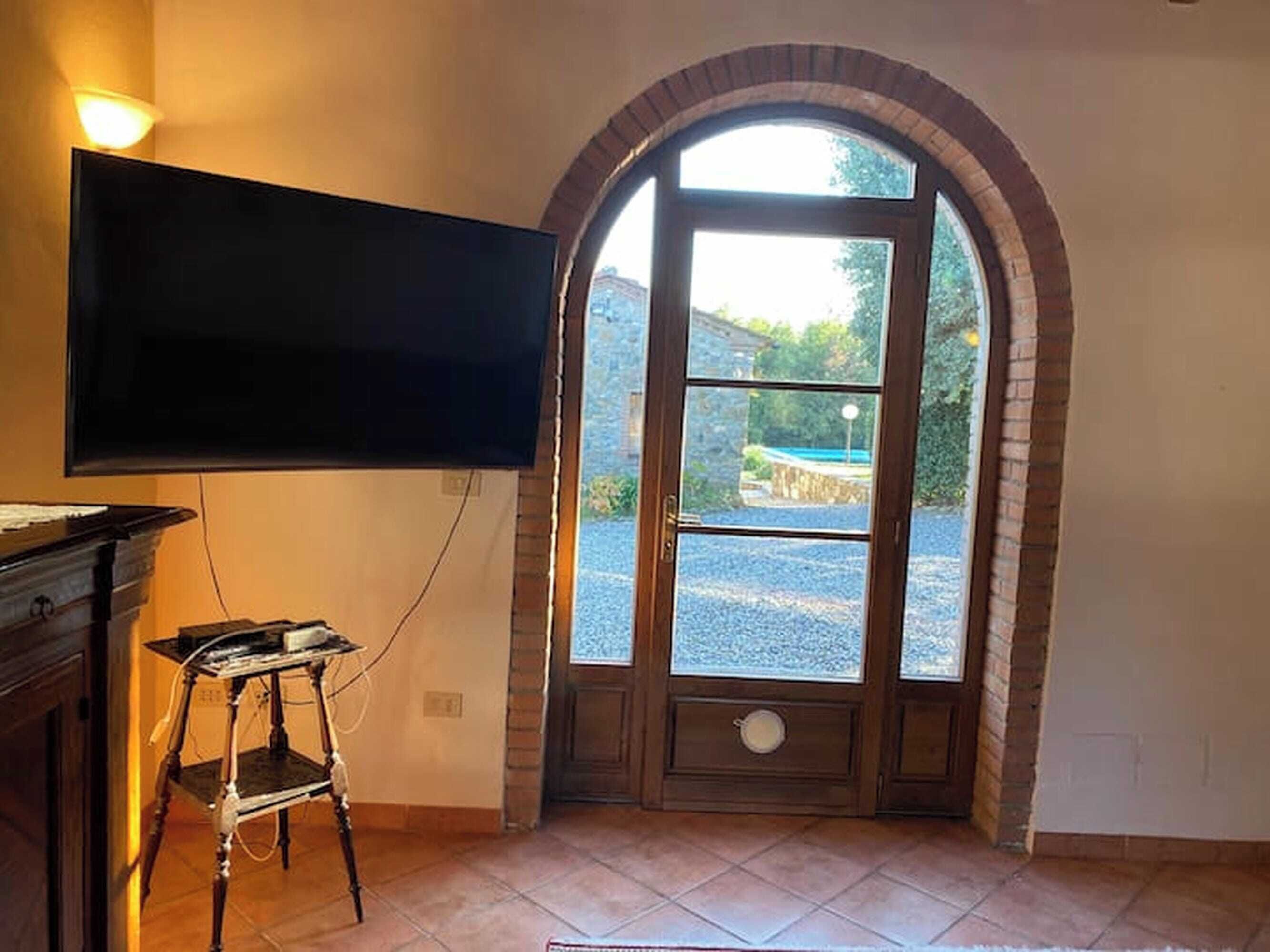 A room with a television mounted on the wall, a wooden door with a window, and a tiled floor.