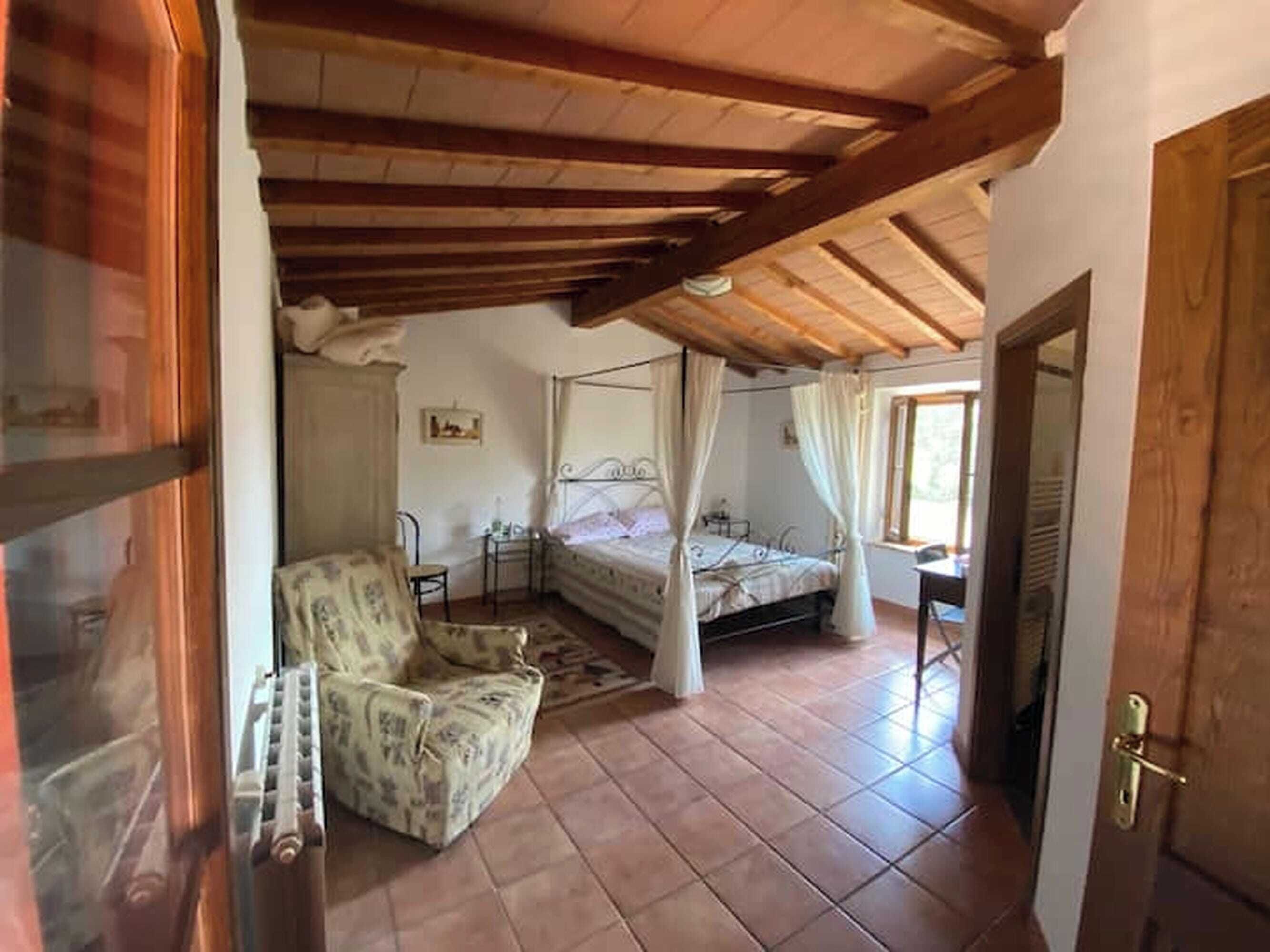 A bedroom with a four-poster bed, a chair, a small table, and a window.