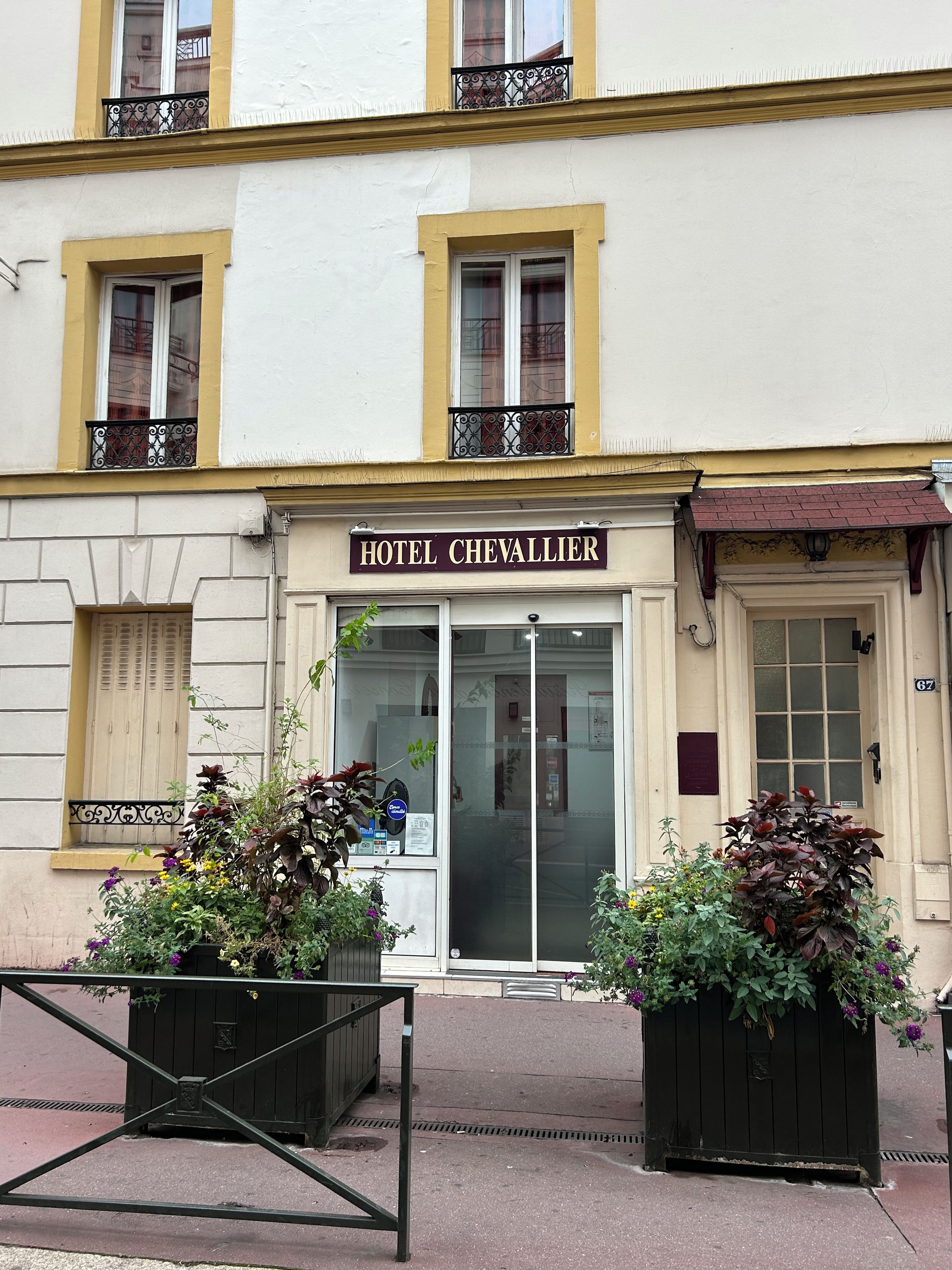 A hotel named 'HOTEL CHEVALLIER' with a classic facade, a glass entrance, and decorative iron railings on the balconies.