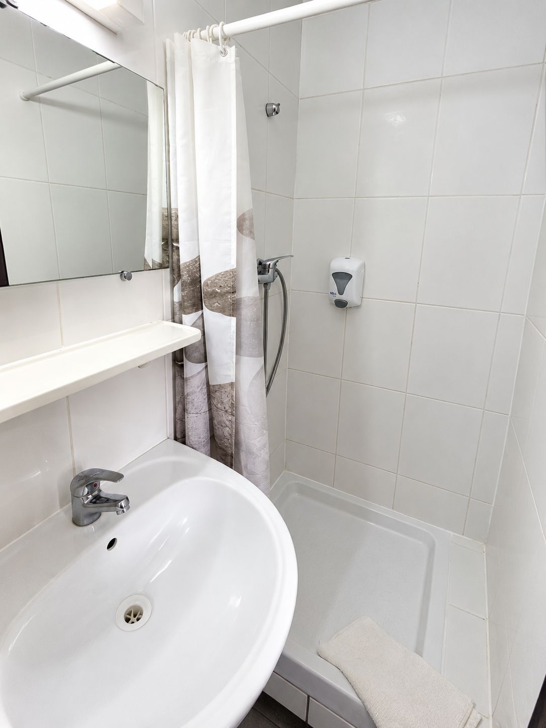 Un baño con lavamanos blanco, espejo, cortina de ducha y cabezal de ducha manual.