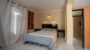 Ein Hotelzimmer mit Bett, Kopfteil, zwei Wandleuchten, einem Vorhang und einer Tür zu einem anderen Raum.