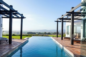 A swimming pool with a view of a landscape, a pergola, and a glass-enclosed area with seating. - Luxury 7-Bedroom Manor on Stellenbosch Wine Estate, Mountain & Vineyard Views (Cape Town)
