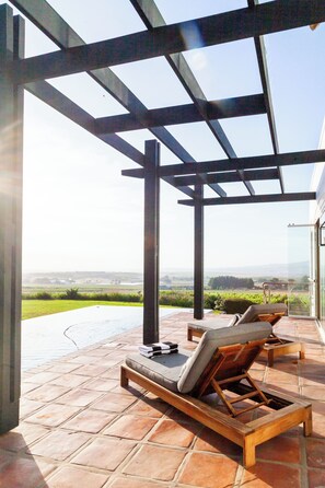 A covered outdoor area with a pool, lounge chairs, and a view of the landscape. - Luxury 7-Bedroom Manor on Stellenbosch Wine Estate, Mountain & Vineyard Views (Cape Town)
