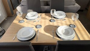 A dining table set for four with white plates, silverware, and wine glasses, surrounded by dark chairs in a modern living room. - Yorkshire Lodge with Hot tub (york)