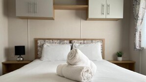 A neatly made bed with rolled towels, a bedside lamp, and a small plant on a bedside table. - Yorkshire Lodge with Hot tub (york)