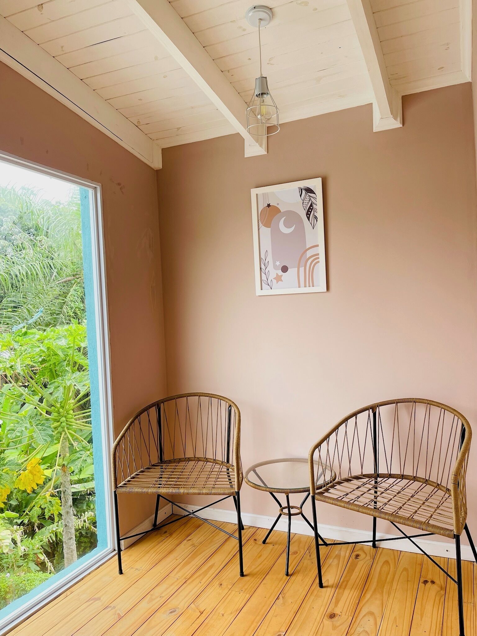 A room with two wicker chairs, a small round table, a ceiling light, and a framed artwork on the wall.