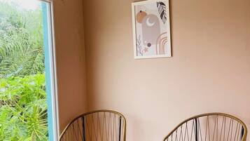 A room with two wicker chairs, a small round table, a ceiling light, and a framed artwork on the wall.