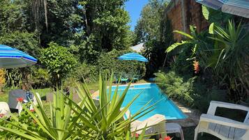 A pool with lounge chairs and umbrellas, surrounded by lush greenery and a brick wall.