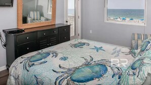 A bedroom with a large bed, a dresser, a mirror, a window with a beach view, and a door leading to a balcony. - Big Surf 1E 2D - Gulf View Beach Pool and Fun (Gulf Shores)