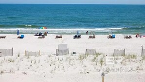 A beach with rows of sun loungers and umbrellas, a fence, and a clear view of the ocean. - Big Surf 1E 2D - Gulf View Beach Pool and Fun (Gulf Shores)