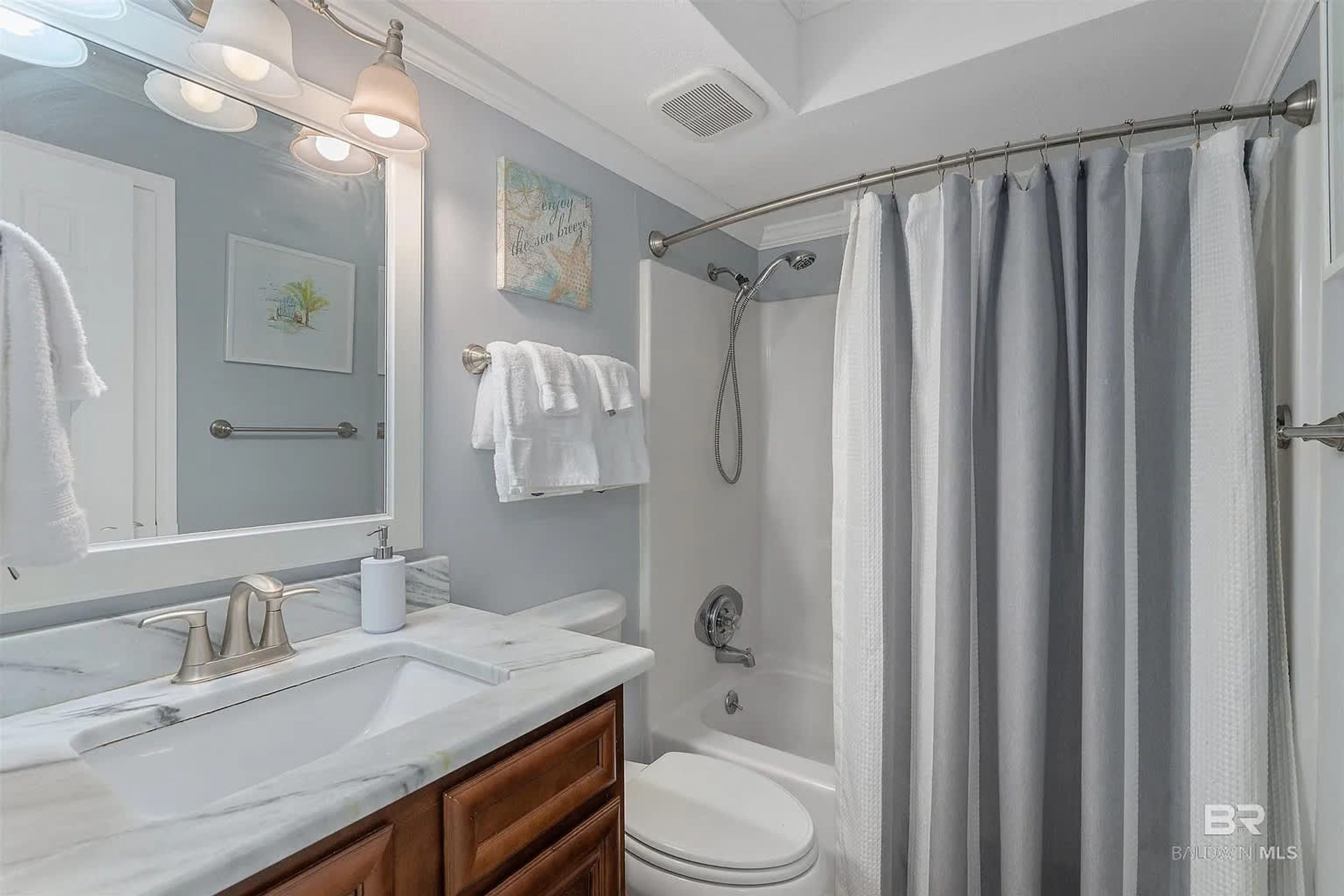 A bathroom with a white sink, a toilet, a shower with a curtain, a mirror, and a towel rack.