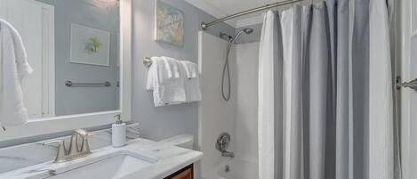 A bathroom with a white sink, a toilet, a shower with a curtain, a mirror, and a towel rack.