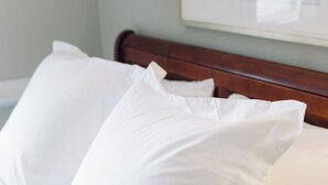 Ein Bett mit weißen und beigen Kissen, ein Holz-Kopfteil und ein gerahmtes Bild an der Wand.