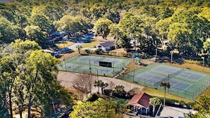 An aerial view of a residential area with multiple tennis courts, houses, and dense greenery.