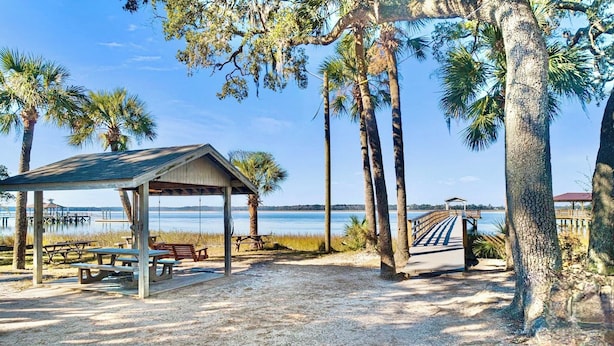 A beachside park with a covered pavilion, picnic tables, and a wooden walkway leading to a dock.
