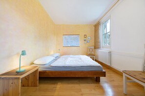 Un dormitorio con una cama de madera, una mesita de noche, un escritorio, un ventanal y un mapa en la pared.