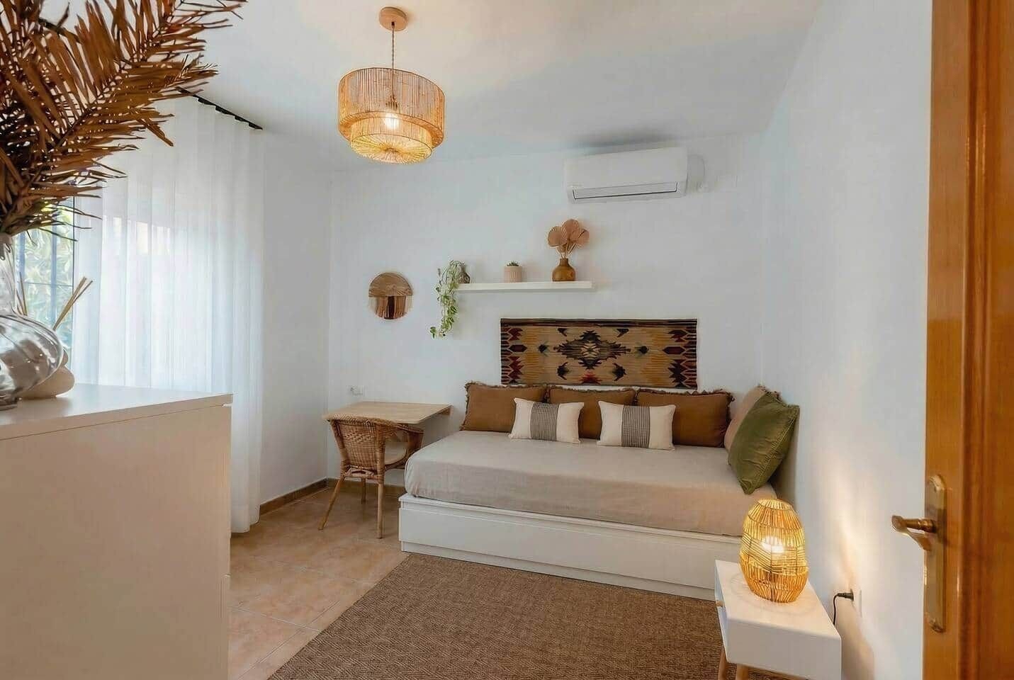 Une chambre à coucher comprenant un lit, un bureau, une chaise, un luminaire suspendu et un climatiseur fixé au mur.