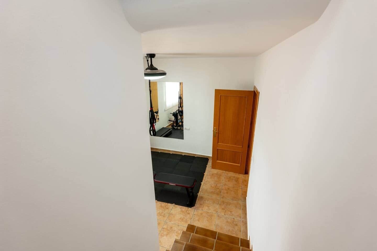 Un pasillo con una puerta de madera, un tapete negro y una lámpara en el techo.