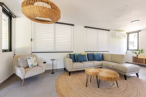 Ein modernes Wohnzimmer mit einer Couch, einem Sessel, einem runden Couchtisch und einer Pendelleuchte.