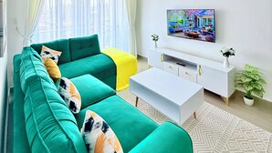 A modern living room with a green sofa, a white coffee table, a ceiling fan, a TV on the wall, and a patterned rug. - The magical view condo kilimani (Nairobi)