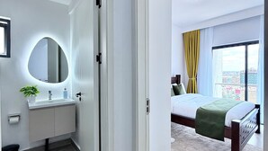 A modern hotel room with a bathroom, a bed, a large window, and a view of the city. - The magical view condo kilimani (Nairobi)