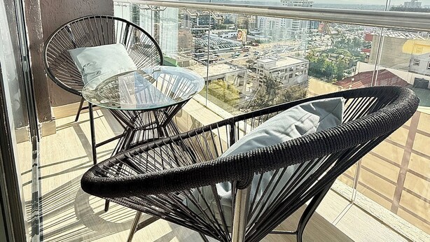 A balcony with a glass table and two wicker chairs, overlooking a cityscape. - The magical view condo kilimani (Nairobi)