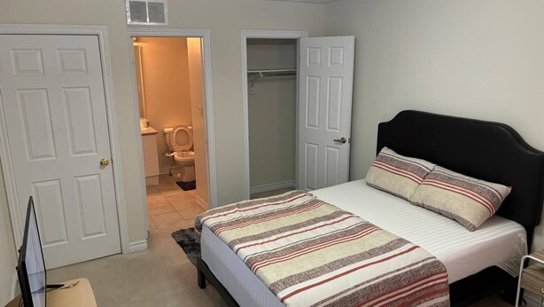 A bedroom with a bed, a nightstand, a TV, and a bathroom visible through an open door. - Room-ensuite Room in 3 Bedroom Townhouse (Brampton)