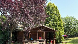 A wooden cabin with a porch, surrounded by lush greenery and trees. - Casale del Sole in the hills of Trevignano: pool and nature 5 min. from the Lake! (Monterosi)